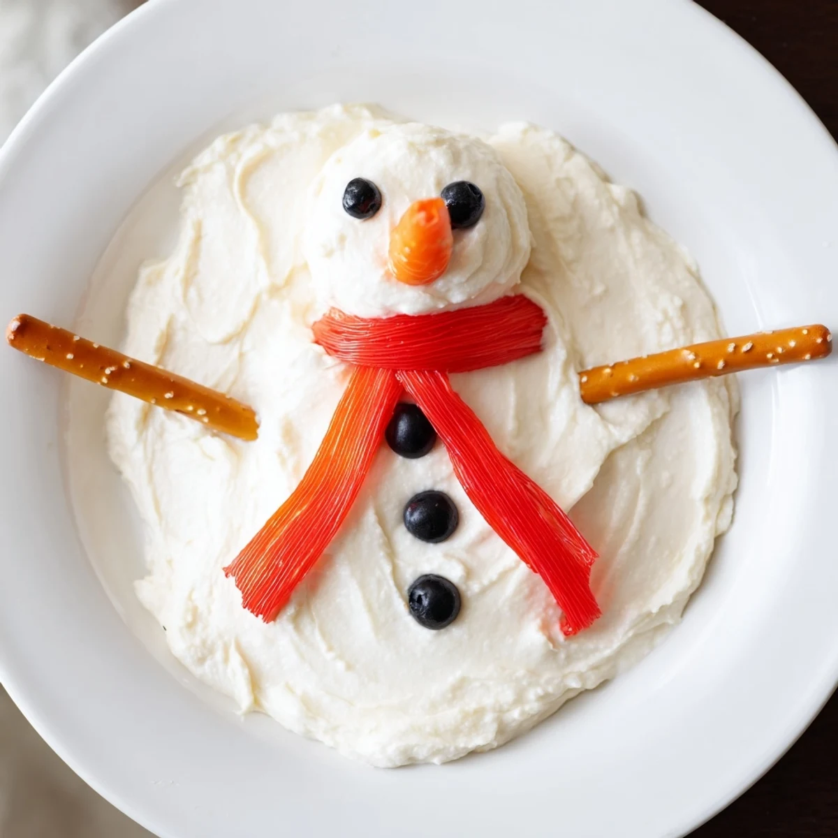 A creamy Melted Snowman Dip, complete with pretzel arms and carrot nose, is ready to serve.