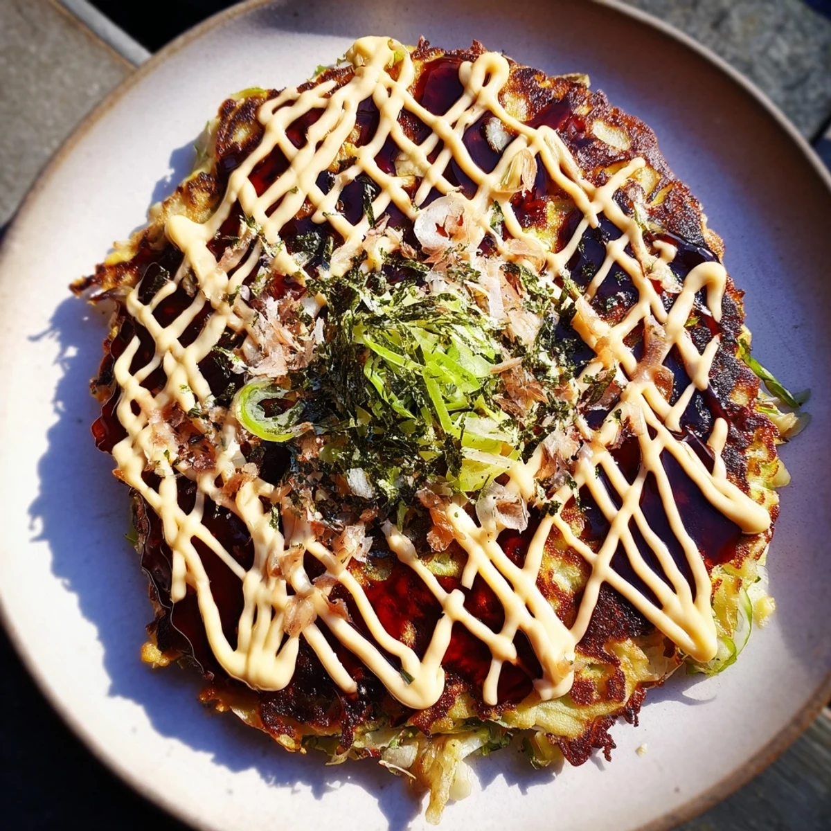 Savory Japanese Okonomiyaki pancake topped with sauce, mayo, and dancing bonito flakes, ready to eat.