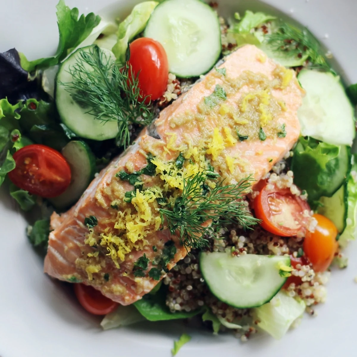Warm Lemon Herb Salmon Salad featuring crisp greens, cherry tomatoes, cucumber, and fluffy quinoa with a zesty lemon dressing.