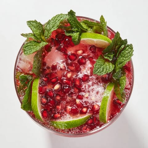 A very sparkly, reddish-pink Pomegranate and Mint Wreath drink with fresh, green mint leaves.