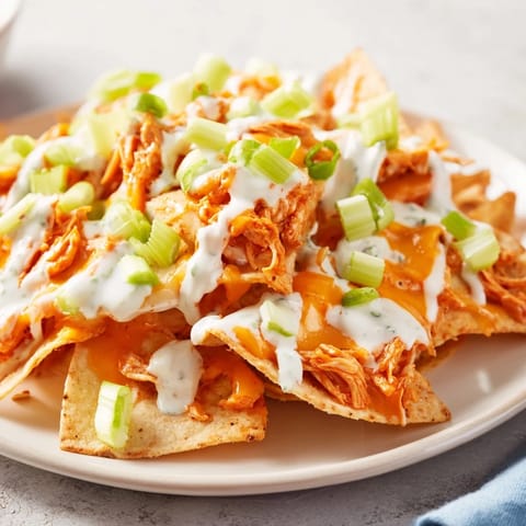 Frisch aus dem Ofen: saftiges Buffalo-Hähnchen auf knusprigen Nachos mit Ranch-Drizzle und Salatgurken-Stücken.
