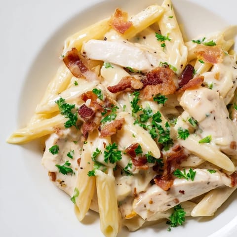 Creamy Chicken Bacon Penne on a rustic table, featuring crispy bacon pieces and creamy sauce with steam rising from the pasta.