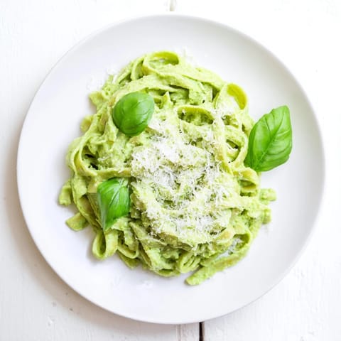 Ein Teller mit Pasta Creamy Green Pea Alfredo, übergossen mit einer cremigen, hellgrünen Sauce und frischen Basilikumblättern.