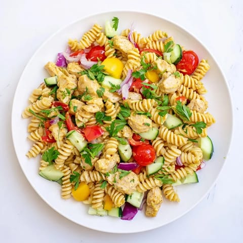 Ein großer Bowl mit Honey Mustard Chicken Pasta Salad, gefüllt mit gekochten Spiralnudeln, saftigem Hühnchenstreifen und buntem Gemüse wie Kirschtomaten und Paprika.