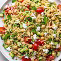 Lemony Chickpea Orzo Salad in a white bowl, tossed with diced cucumber, halved tomatoes, and herbs, garnished with crumbled feta and lemon zest.